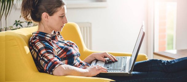 Woman sitting on yellow sofa in the living room and using laptop - Foto, Bild