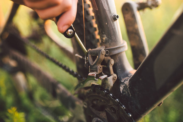 χέρι με ένα εργαλείο ποδηλάτων ήταν που ασχολούνται με τον καθορισμό ένα ποδήλατο σε εξωτερικούς χώρους στο ηλιοβασίλεμα - Φωτογραφία, εικόνα