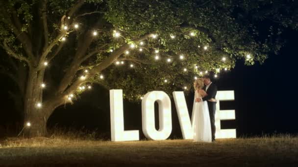 Молодая пара влюбленных в вечерние платья танцуют возле любовных светлых букв
. - Кадры, видео