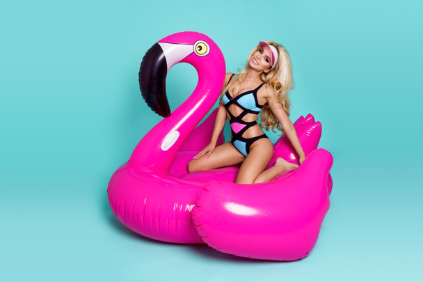 Stunning sexy blonde model in a colorful bikini, lies on a pink flamingo - Foto, Bild