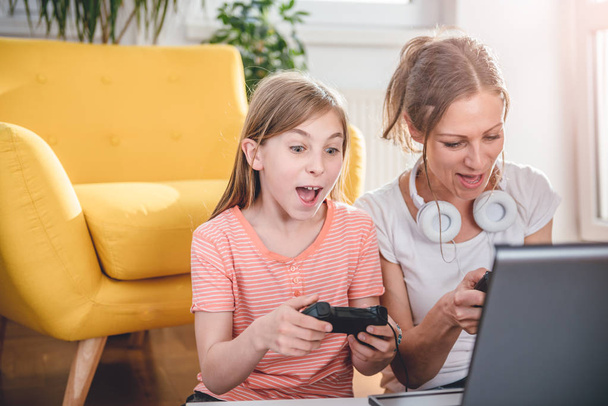 Mother and daughter playing video games on laptop at home - Foto, immagini