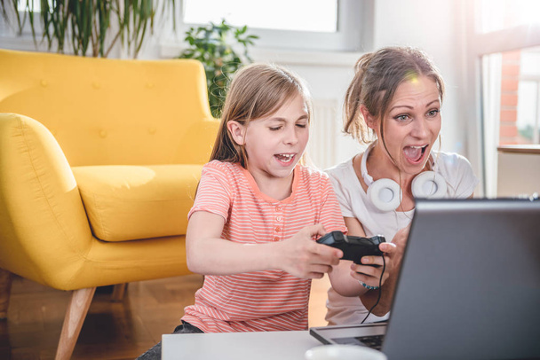 Mother and daughter playing video games on laptop at home - Photo, Image