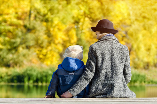 Blond garçon et sa mère dans le chapeau assis sur le quai. Vue arrière
 - Photo, image