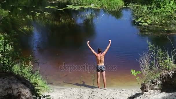 Thin man doing exercises on the shore of wild river - Footage, Video