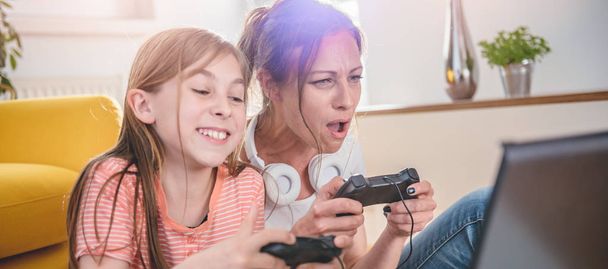 Mother and daughter playing video games on laptop at home - Foto, afbeelding