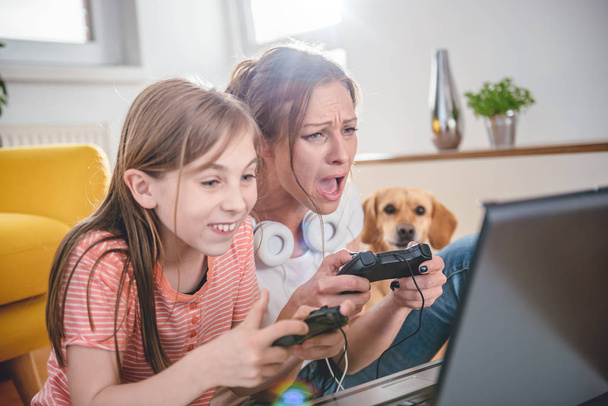 Mother and daughter playing video games on laptop at home - 写真・画像