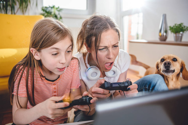 Mother and daughter playing video games on laptop at home - Valokuva, kuva