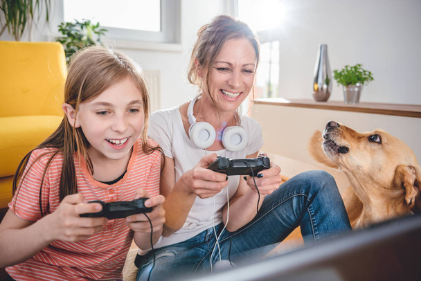 Mother and daughter playing video games on laptop at home - Photo, image