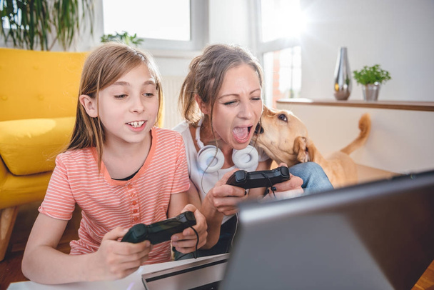 Mother and daughter playing video games on laptop at home - Фото, изображение