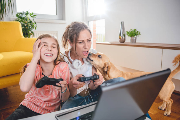 Mother and daughter playing video games on laptop at home - Zdjęcie, obraz