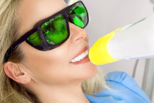 Молодая красивая женщина с красивыми белыми зубами сидит на стоматологическом стуле. Зубной врач лечит ее зубы
. - Фото, изображение