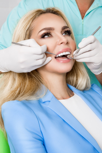 Giovane bella donna con bellissimi denti bianchi seduti su una sedia dentale. Il dentista si cura i denti
. - Foto, immagini