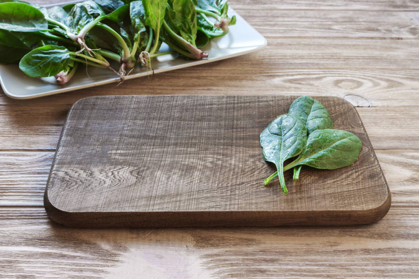 cutting board on a table with spinach leaves, a plate of spinach in the background. Meal preparation concept - Foto, immagini