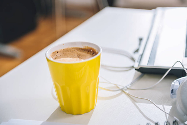 Yellow cup of coffee on the table by the laptop in the office - Fotoğraf, Görsel