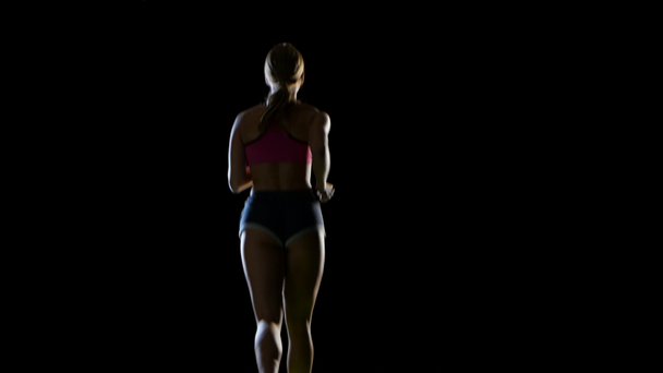 Atlética mujer fitness corriendo vista trasera sobre un fondo negro. Silueta
 - Imágenes, Vídeo