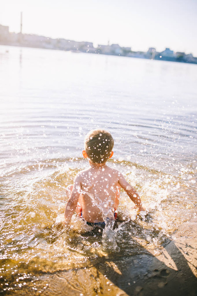 chłopiec dziecko gra sprawia, że plamy, bije ręce na wody w rzece o zachodzie słońca - Zdjęcie, obraz