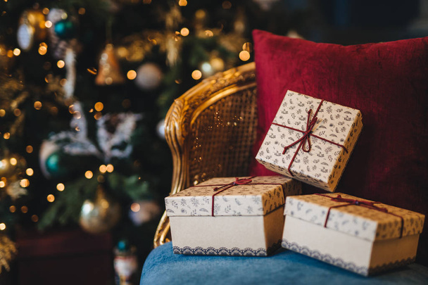 Imagen de las cajas de regalo envueltas se encuentran en el sillón contra el fondo decorado del árbol de Año Nuevo. Preparación para las vacaciones. Hermoso árbol de Navidad con guirnaldas y regalos en interiores
 - Foto, imagen