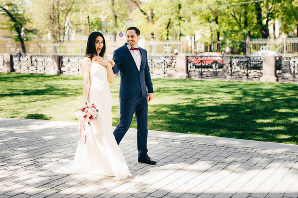 Эмоциональная невеста в белом длинном платье проводит свадебный букет ходить вместе с женихом, любоваться красивой природой, имеют приятные выражения, как отпраздновать свою свадьбу с родственниками
 - Фото, изображение