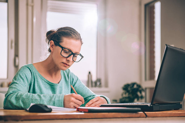 Woman wearing eyeglasses sitting at a desk at home and doing paperwork - Photo, Image