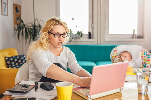 Mãe vestindo óculos trabalhando no escritório em casa no laptop e cuidando de seu bebê
 - Foto, Imagem