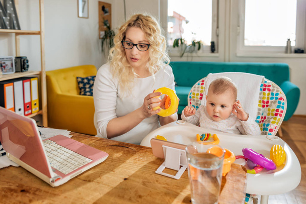 Mãe vestindo óculos trabalhando no escritório em casa no laptop e cuidando de seu bebê
 - Foto, Imagem