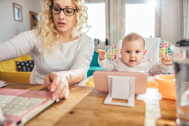 Anya visel szemüveget office laptop otthoni munkavégzés, és a baba gondozása - Fotó, kép