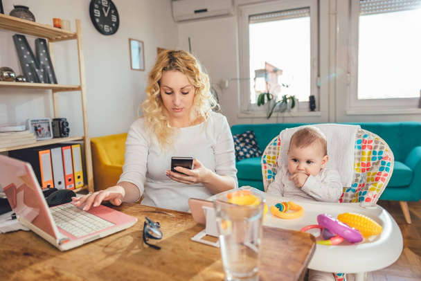 Mãe trabalhando no escritório em casa usando telefone inteligente e cuidar de seu bebê
 - Foto, Imagem