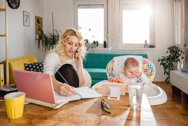 Anya beszél szúró telefon és írásban le jegyzetek az otthoni iroda, és a baba gondozása - Fotó, kép
