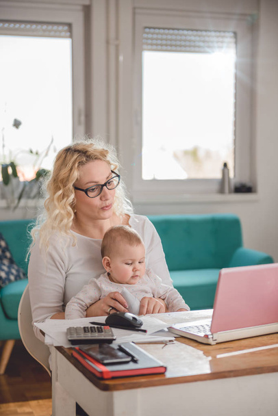 Mutter mit Brille hält Baby in der Hand und öffnet Umschlag im Home Office - Foto, Bild