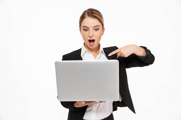 Shocked blonde business woman holding laptop computer - 写真・画像