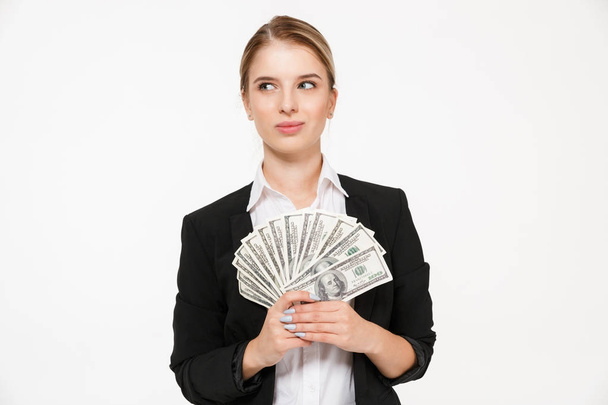 Smiling pensive blonde business woman holding money and looking away - Fotó, kép