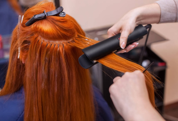 Κομμωτήριο κάνει χτένισμα κορίτσι με μακριά κόκκινα μαλλιά στο σαλόνι ομορφιάς. - Φωτογραφία, εικόνα