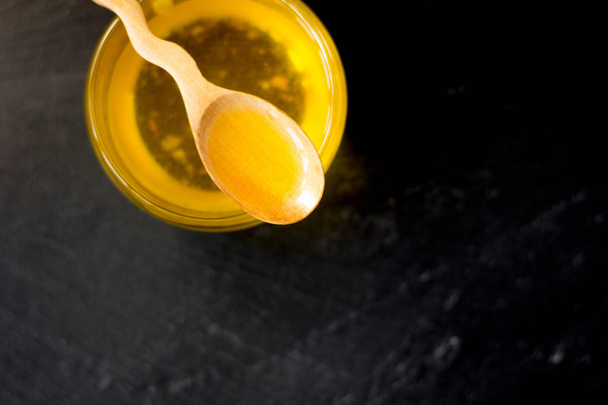 Fresh ghee butter in a wooden spoon over black stone background. - Photo, Image