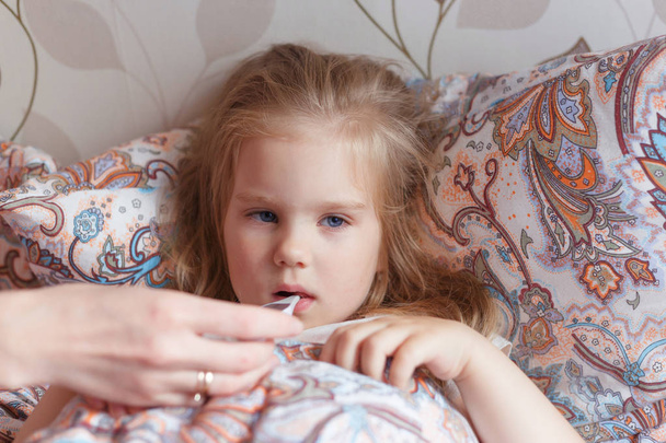 Холодна дівчинка лежить в сумному ліжку, вимірюючи температуру в роті
 - Фото, зображення