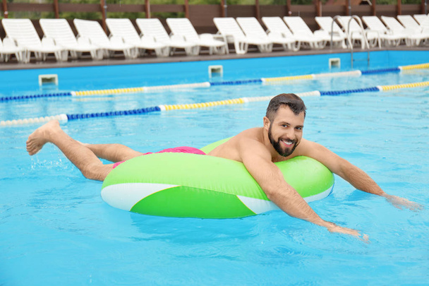 Handsome young man with inflatable ring relaxing in blue swimming pool - Foto, immagini