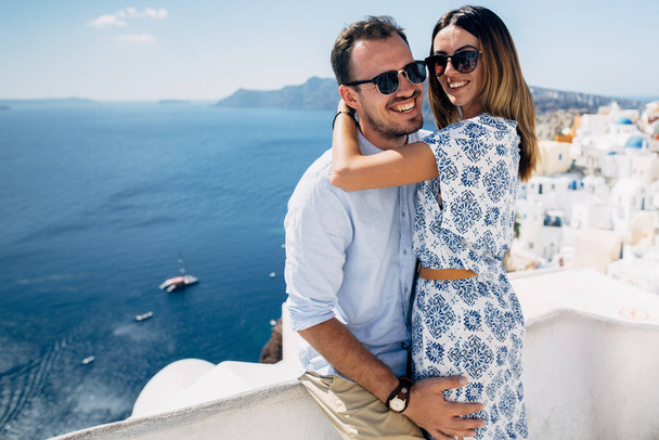 Pareja feliz abrazándose y riendo juntos con una vista de Santorini
 - Foto, Imagen