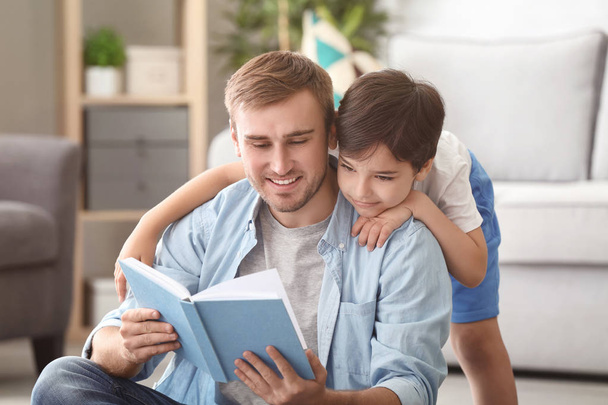 Young man and his little son reading book at home - Foto, imagen