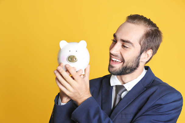 Young man with piggy bank on color background - Foto, imagen
