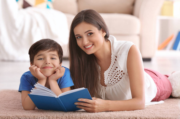 Mujer joven y su pequeño hijo leyendo libro en casa
 - Foto, Imagen