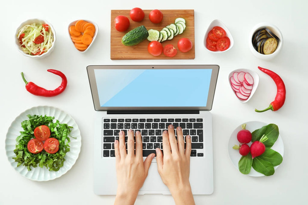 Woman using laptop near vegetables on white background. Food blogger concept - Fotó, kép