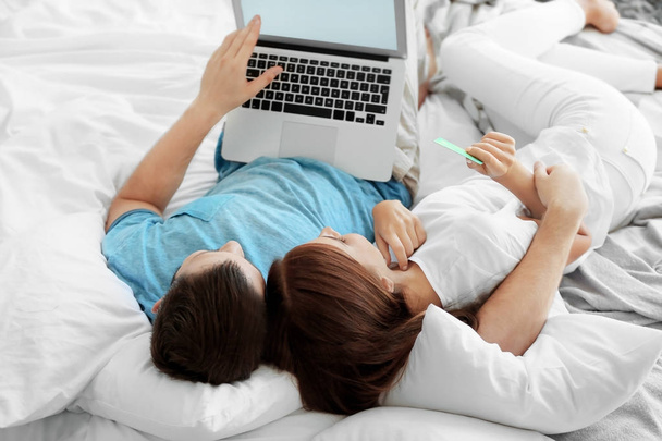 Young couple with laptop lying on bed at home. Internet shopping concept - Fotografie, Obrázek