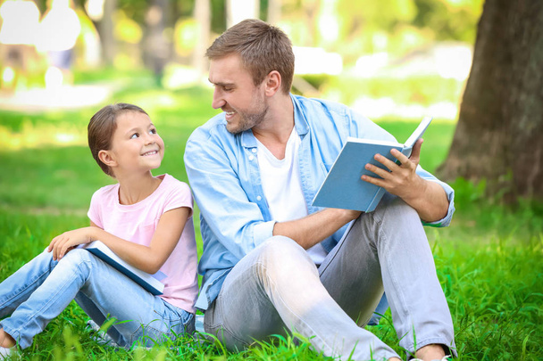 Young man and his little daughter reading books in park - Valokuva, kuva