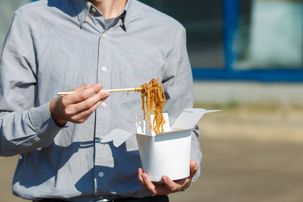 Handsome man with chinese noodles in box with shrimp, vegetables and sesame with soy sauce. Food concept. - 写真・画像