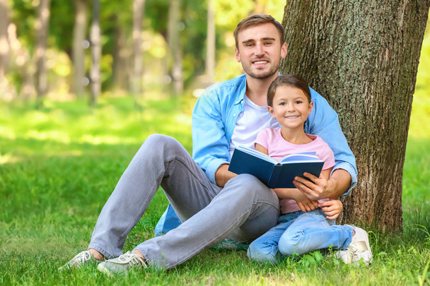 Young man and his little daughter reading book in park - Фото, зображення