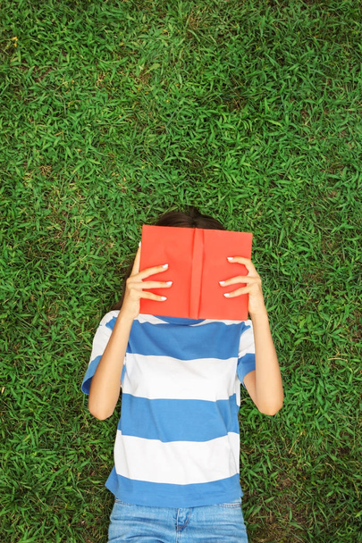 Teini tyttö kirja makaa vihreällä ruoholla
 - Valokuva, kuva