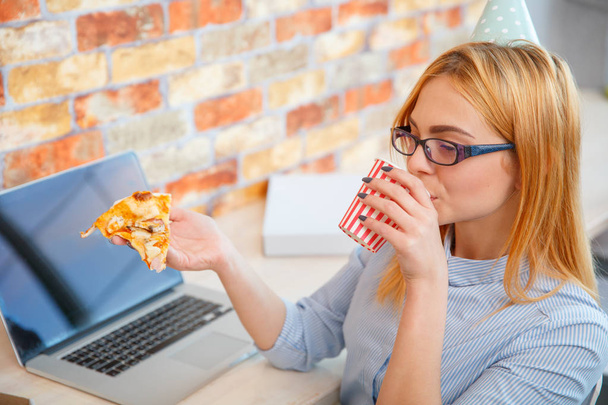 A girl eating pizza in the office in front of a laptop - Foto, Imagem