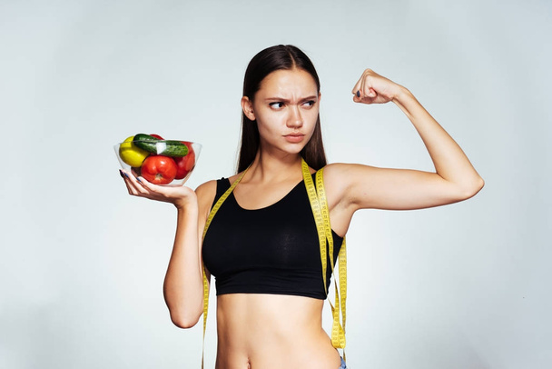 une jeune belle fille sportive regarde sa silhouette, tient une assiette avec des légumes et des fruits faibles en calories dans ses mains
 - Photo, image
