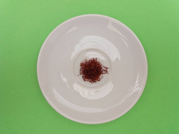 azafrán sin moler en un plato blanco sobre fondo verde
 - Foto, Imagen