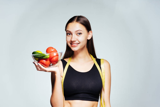 молодая красивая девушка следит за своим здоровьем и фигурой, держа в руках тарелку с полезными овощами и фруктами
 - Фото, изображение