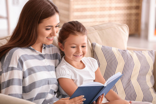 Young woman and her little daughter reading book at home - Foto, Imagen